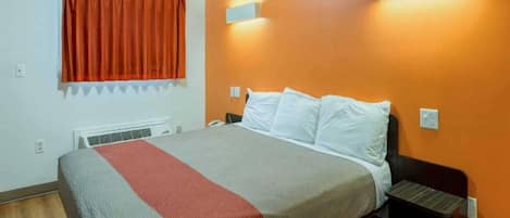 Una habitación de hotel con cama, mesita de noche, ventana con cortinas y una lámpara de pared.
