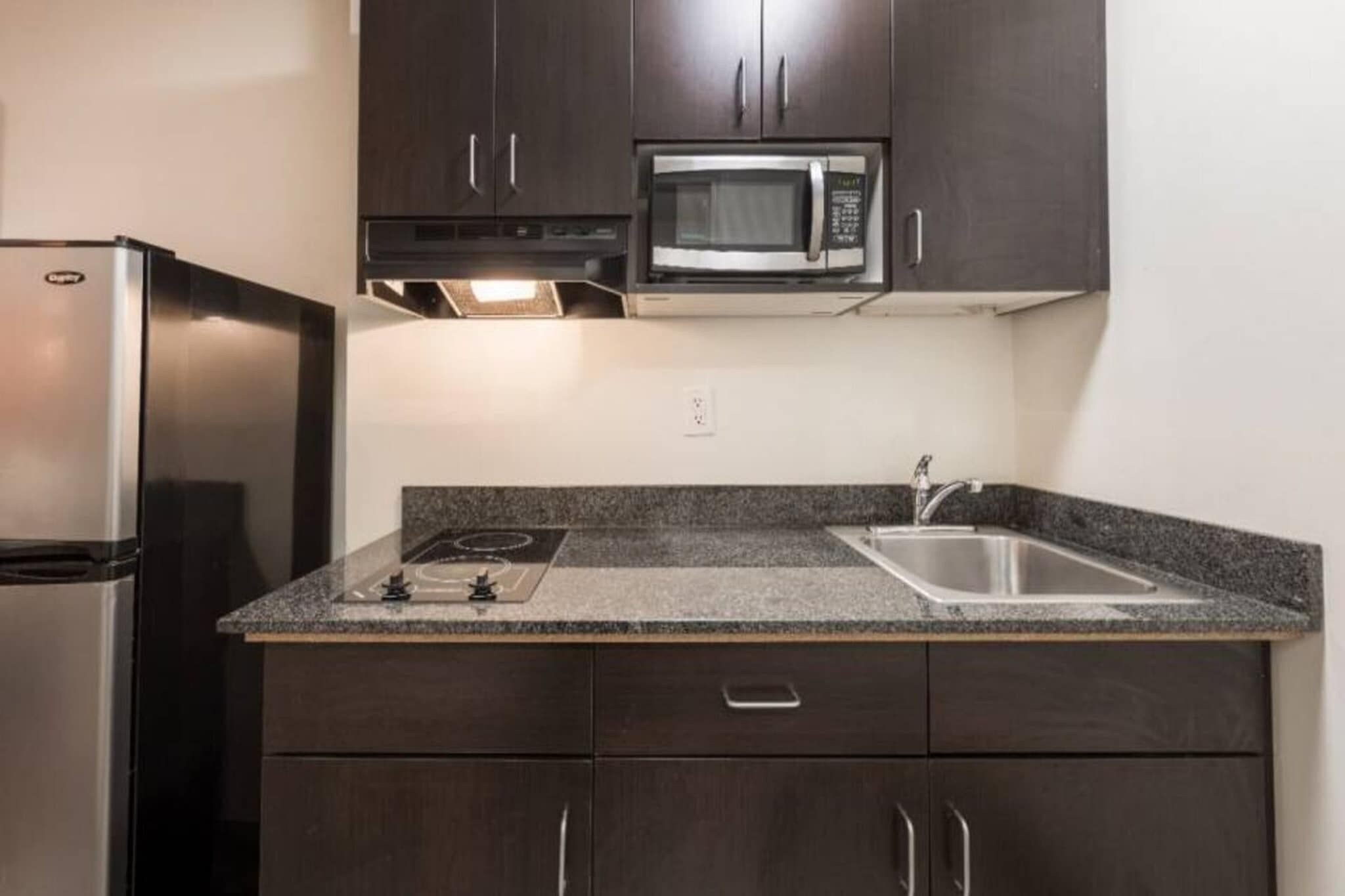 A compact kitchen with a refrigerator, microwave, sink, and dark wooden cabinets.