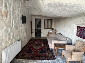 A cozy living room with a stone wall, a beige sofa, a wooden coffee table, and a patterned rug. - Leyla Cave House (Nevsehir)