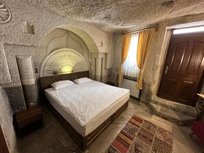A room with a bed, a stone wall, a wooden door, and a patterned rug. - Leyla Cave House (Nevsehir)