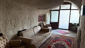 A cozy room with a stone wall, a beige sofa, a patterned rug, and a large window. - Leyla Cave House (Göreme)