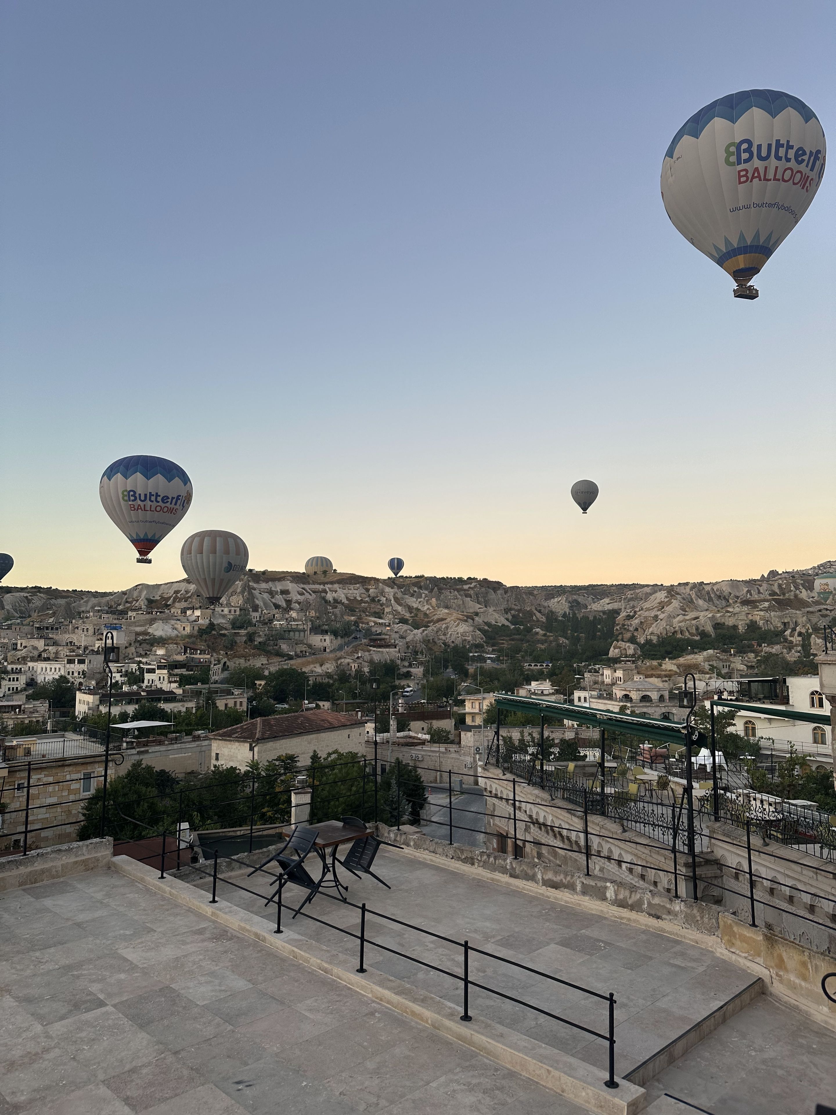 A view of a town with multiple hot air balloons in the sky and a staircase leading to a terrace.
