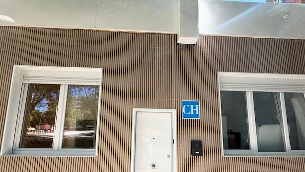 Fachada de um edifício com ripas verticais de madeira, uma porta branca e uma placa azul com a letra 'CH'.