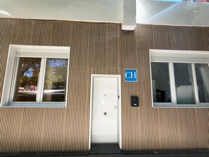 A building facade with vertical wooden slats, a white door, and a blue sign with the letter 'CH'.
