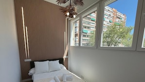 Quarto com cama, parede de ripas de madeira, janela e vista para edifícios.