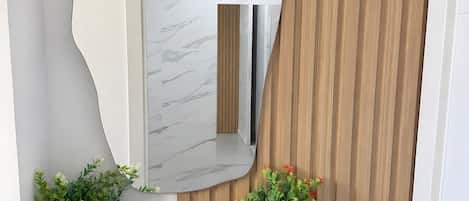 A wall-mounted mirror with a marble-like surface, flanked by two potted plants with green foliage and red flowers.
