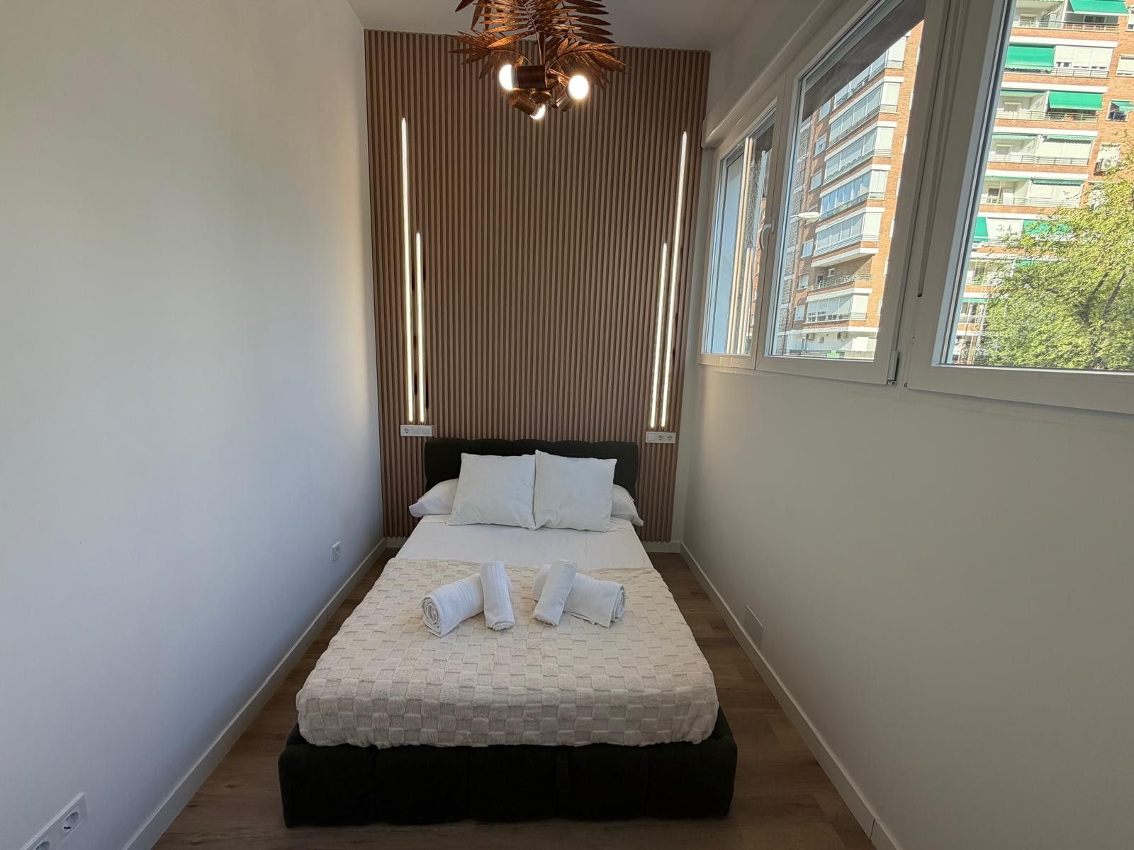 Ein schmales Hotelzimmer mit einem Bett, einem Fenster und einer modernen Leuchte.