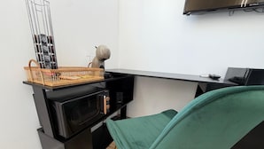 Uma cozinha compacta com micro-ondas, uma cesta de objetos e uma cadeira.