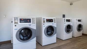 A row of four white front-loading washing machines in a room with wooden flooring and white walls.