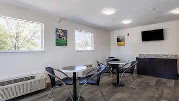 A room with a round table, chairs, a flat-screen TV mounted on the wall, and a window with a view of trees.