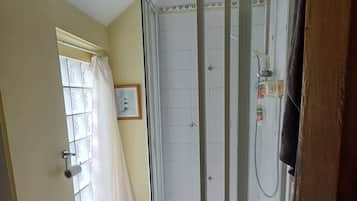 A bathroom with a shower enclosure, toilet, and a window with curtains.
