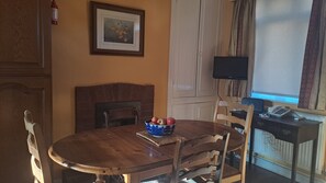 A dining area with a wooden table, chairs, a bowl of apples, a fireplace, and a television on a stand.