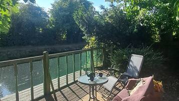 Un espace extérieur aménagé avec une table et des chaises, une clôture verte et une vue sur une étendue d’eau.