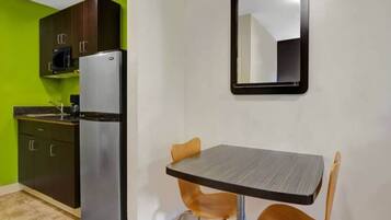 A compact kitchen with a refrigerator, cabinets, and a dining table with chairs.