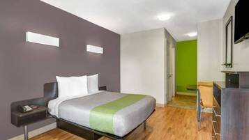 Quarto de hotel com cama, mesa de cabeceira e escrivaninha com cadeira.