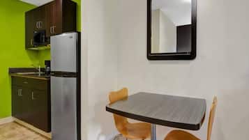 Cocina compacta con refrigerador, microondas y armarios. Cuenta con una pequeña mesa de comedor y dos sillas.