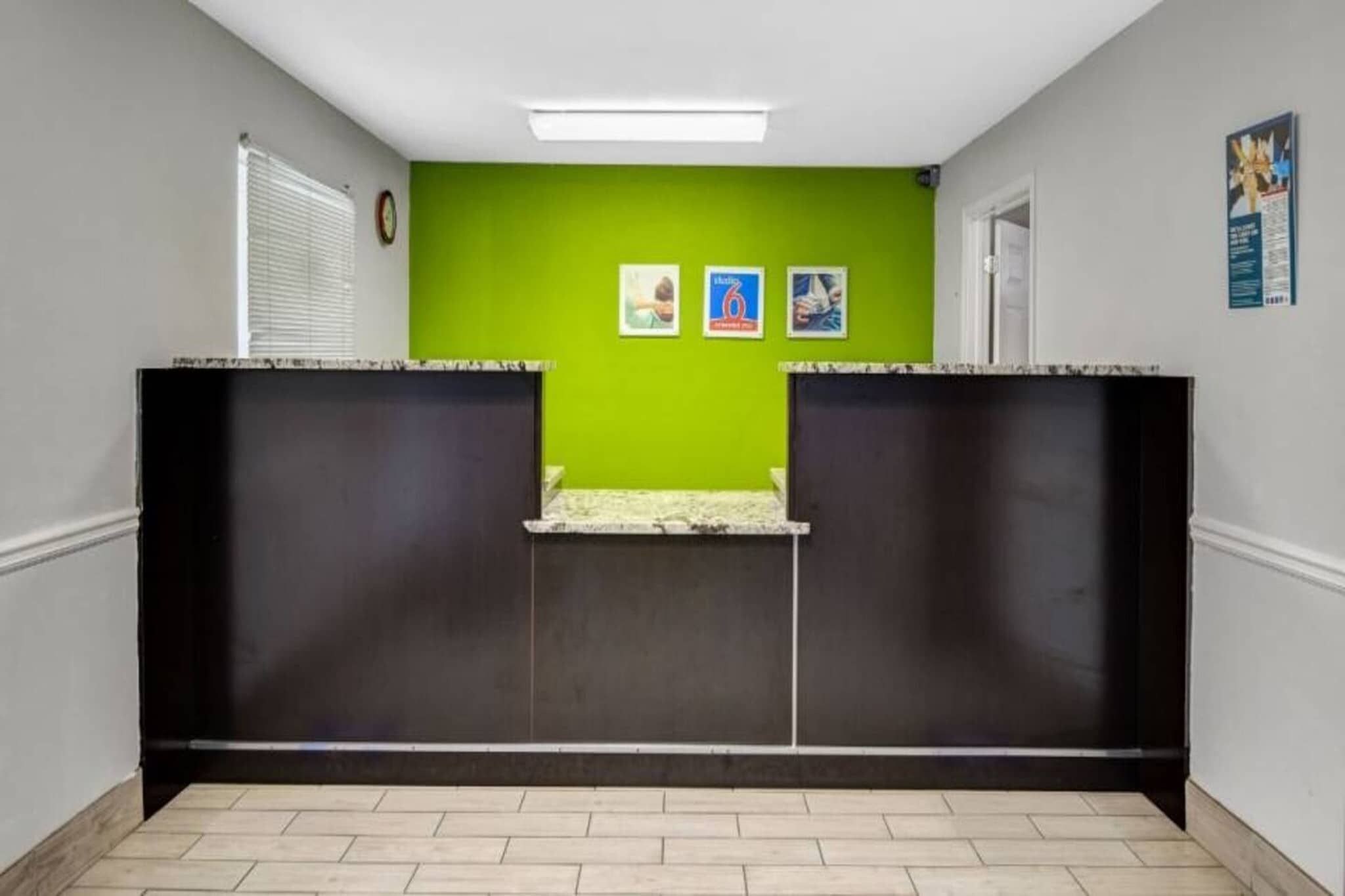 Uma área de recepção com uma parede verde, duas imagens emolduradas, um relógio e uma porta.
