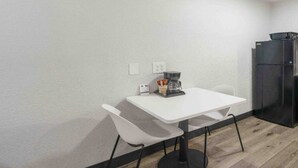 Una habitación pequeña y sencilla con una mesa blanca, dos sillas, una cafetera y un refrigerador.
