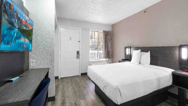 Habitación de hotel con cama, escritorio, televisor y ventana con cortinas.