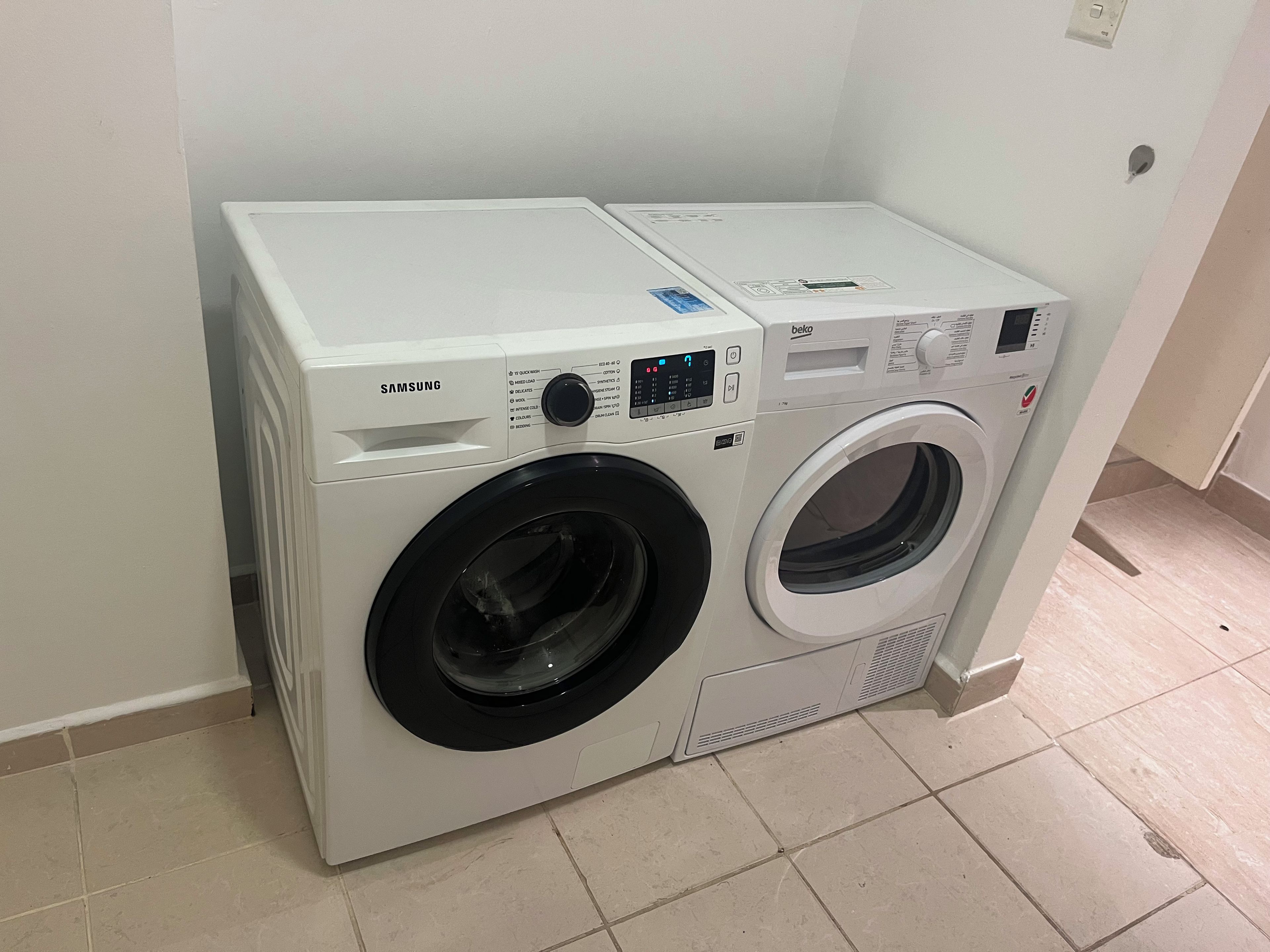 A front-loading Samsung washer and dryer unit with a control panel, located in a room with tiled flooring.