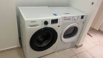 A front-loading Samsung washer and dryer unit with a control panel, located in a room with tiled flooring.