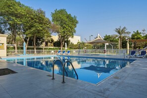 Une piscine à l’eau d’un bleu cristallin, entourée d’une clôture blanche et ombragée par des arbres et une tonnelle.