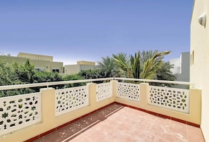 Un balcó amb barana blanca i dibuixos, un paviment de rajoles i vista cap a edificis i zones verdes veïnes.