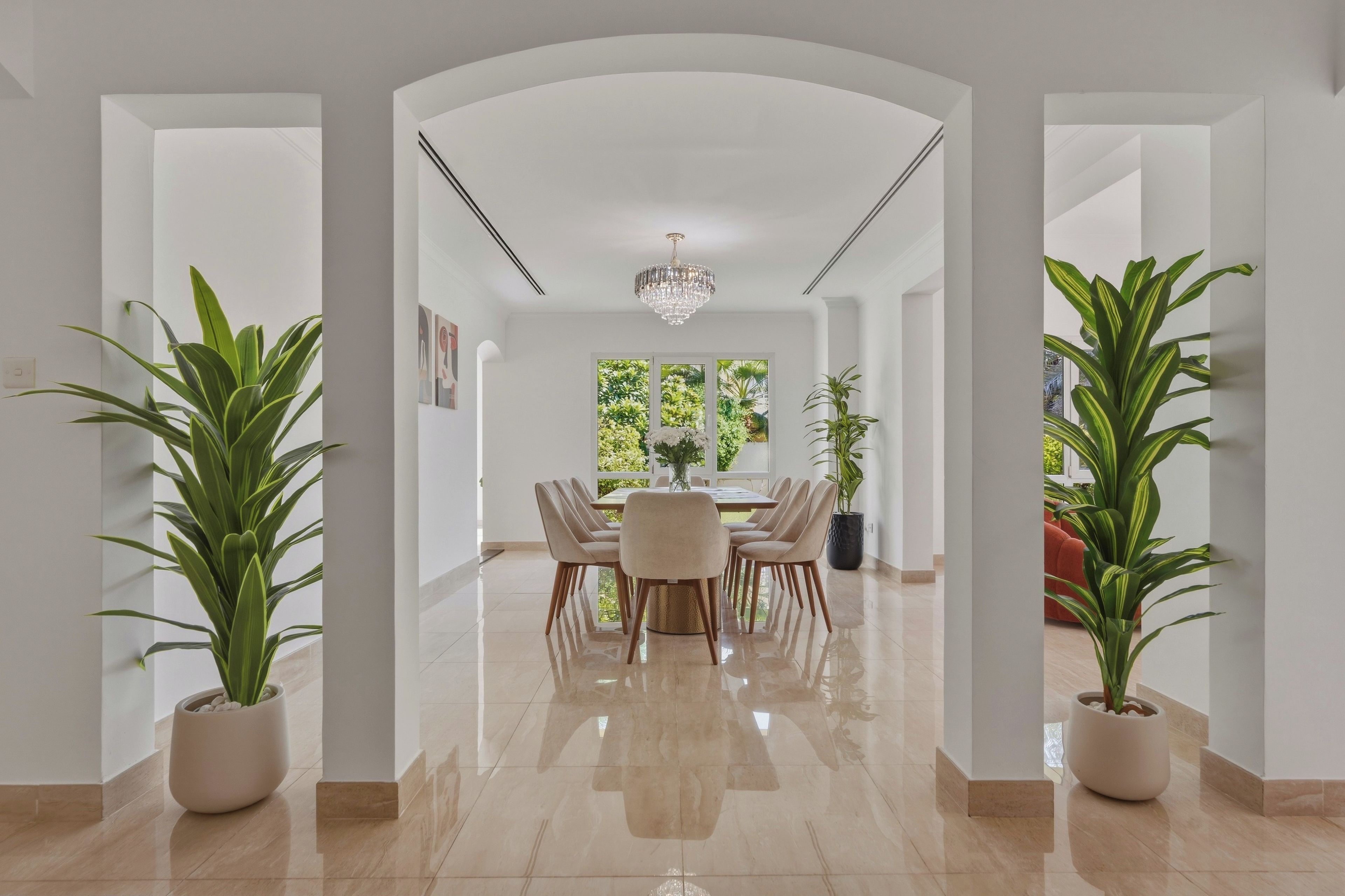 A modern dining area with a chandelier, a table with chairs, and potted plants.