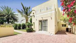A modern two-story building with a paved courtyard, palm trees, and a well-maintained garden. - 5 bedroom villa with direct access to Montgomerie Golf - Perfect for families (Dubai)