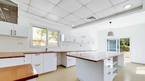 A modern kitchen with white cabinetry, a central island, and a window providing natural light. - 5 bedroom villa with direct access to Montgomerie Golf - Perfect for families (Dubai)