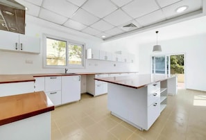 Une cuisine moderne avec des meubles blancs, un îlot central et une fenêtre qui laisse entrer la lumière naturelle.