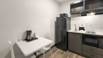 A compact kitchenette with a white table, a black refrigerator, and a coffee maker.