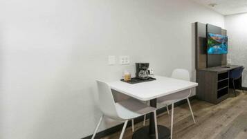 A small room with a white table, two white chairs, a coffee maker, and a television on a stand.