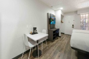 Une pièce de taille modeste, avec un bureau blanc, une chaise, un lit et un téléviseur fixé au mur.