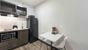 A compact kitchen with a microwave, oven, refrigerator, and a small dining table with chairs. - 2 Beds | Smoking, Deluxe (Tucker)