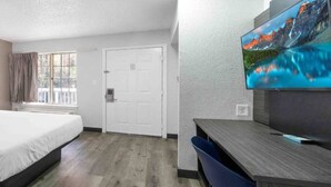 A hotel room with a bed, a desk, a chair, a television, and a door. - 2 Beds | Smoking, Deluxe (Tucker)