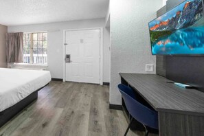 A hotel room with a bed, a desk, a chair, a television, and a door. - 2 Beds | Smoking, Deluxe (Tucker)