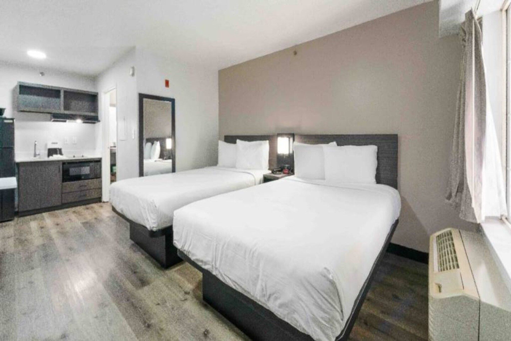 A hotel room with two beds, a kitchenette, and a bathroom.