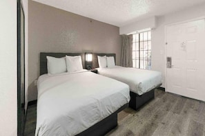 Een hotelkamer met twee bedden, een groot raam en een deur.