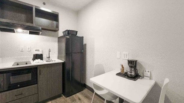 Cocina compacta con refrigerador, horno y lavamanos. Hay una pequeña mesa de comedor con sillas.
