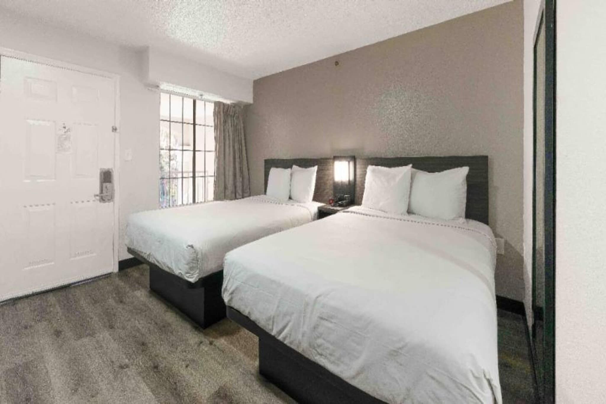 A hotel room with two beds, a door, and a window.
