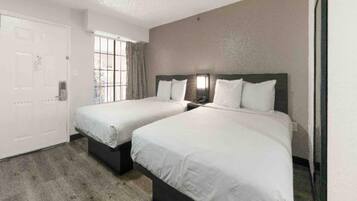 A hotel room with two beds, a door, and a window.