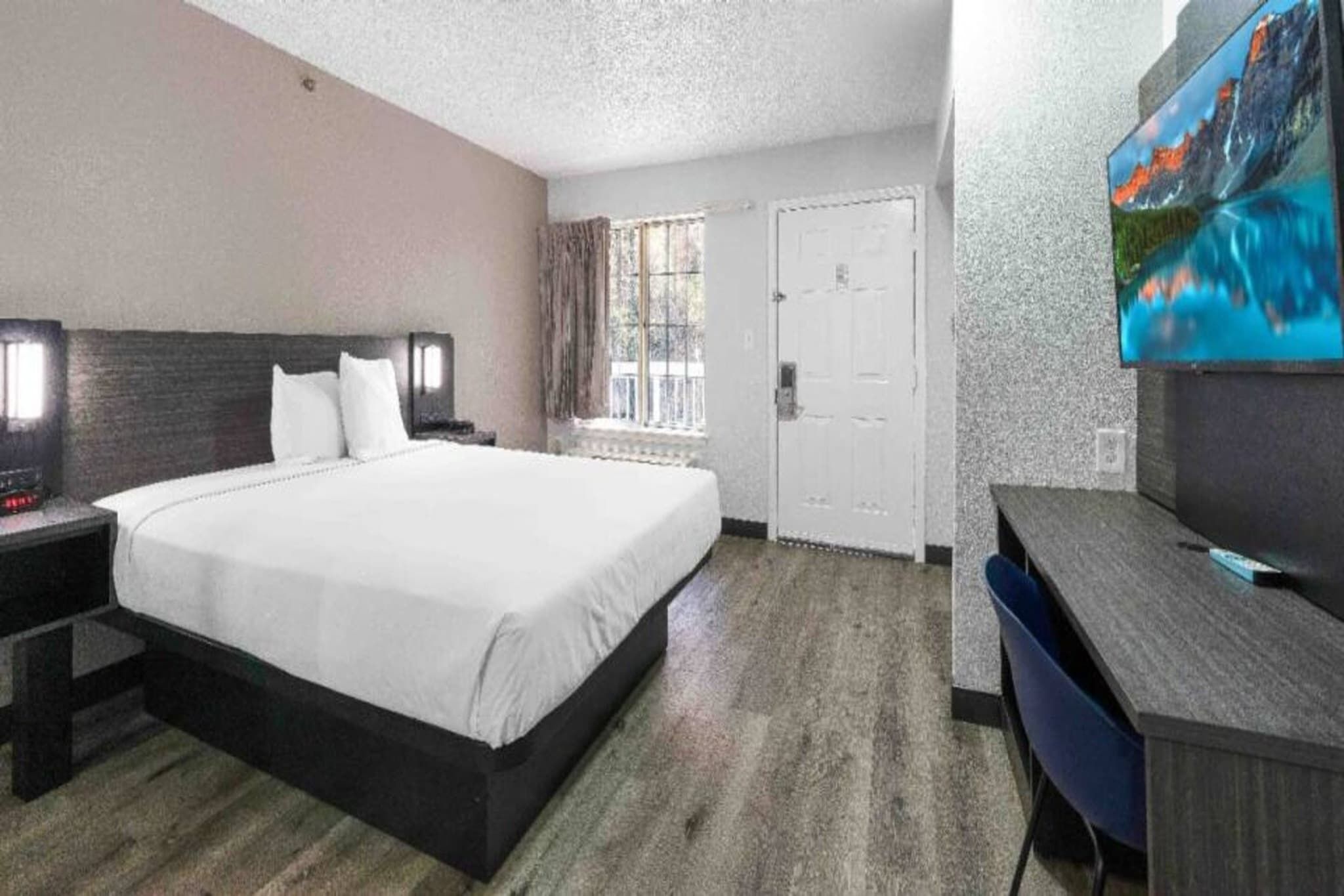 Habitación de hotel con una cama grande, un escritorio, un televisor y una ventana con cortinas.