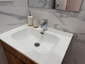 A bathroom with a white sink, a chrome faucet, and a marble backsplash.