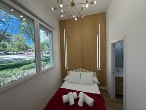 A modern bedroom with a large window, a bed with white linens, a red throw blanket, and a unique ceiling light fixture.