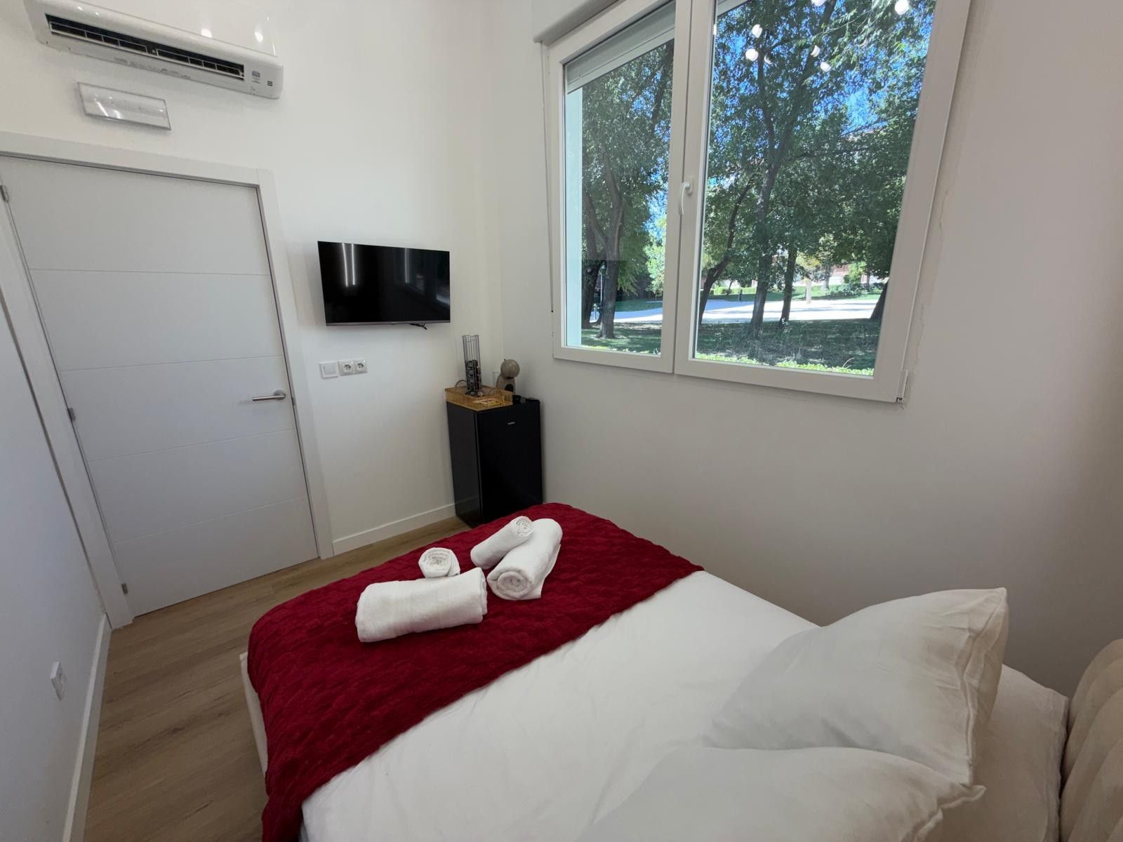 Ein Hotelzimmer mit einem Bett, einem Fernseher, einem Fenster mit Blick auf Bäume und einer Klimaanlage.