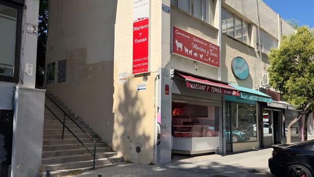 Un edificio con una escalera que lleva a la entrada, un escaparate con señalización y un coche estacionado.