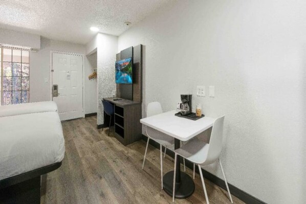 Habitación de hotel compacta con cama, kitchenette pequeño, mesa de comedor con sillas y televisor montado en la pared.