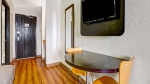 A room with a wooden floor, a dining table with chairs, a television mounted on the wall, and a door. - 2 Queen Beds | Non-Smoking, Mini Fridge (Moriarty)