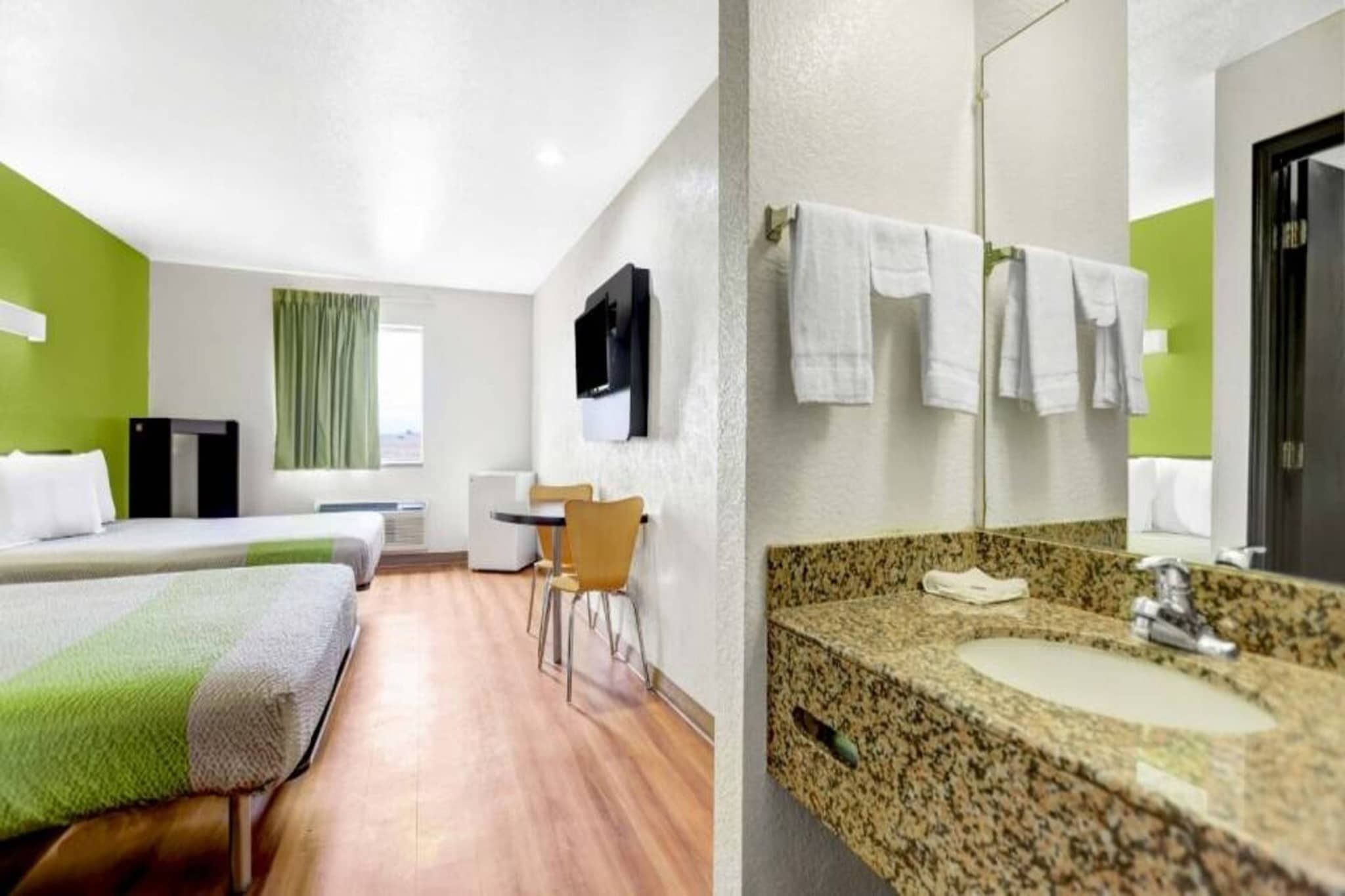 Une chambre d’hôtel avec deux lits, un bureau, une chaise, une télévision et une salle de bain équipée d’un lavabo et d’un miroir.